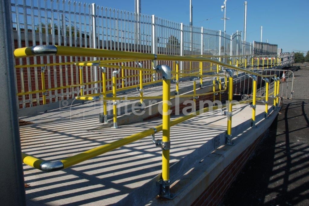 Train station disabled access ramp constructed with Interclamp Key Clamp DDA Assist fittings and bright yellow handrail tube, offering clear guidance and support for disabled passengers.